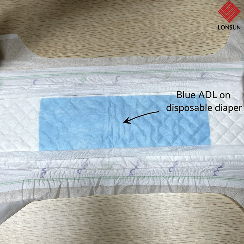 Unfolded baby diaper showing the ADL (Acquisition Distribution Layer) as a white fibrous sheet between the soft topsheet and absorbent core, demonstrating its physical location and texture